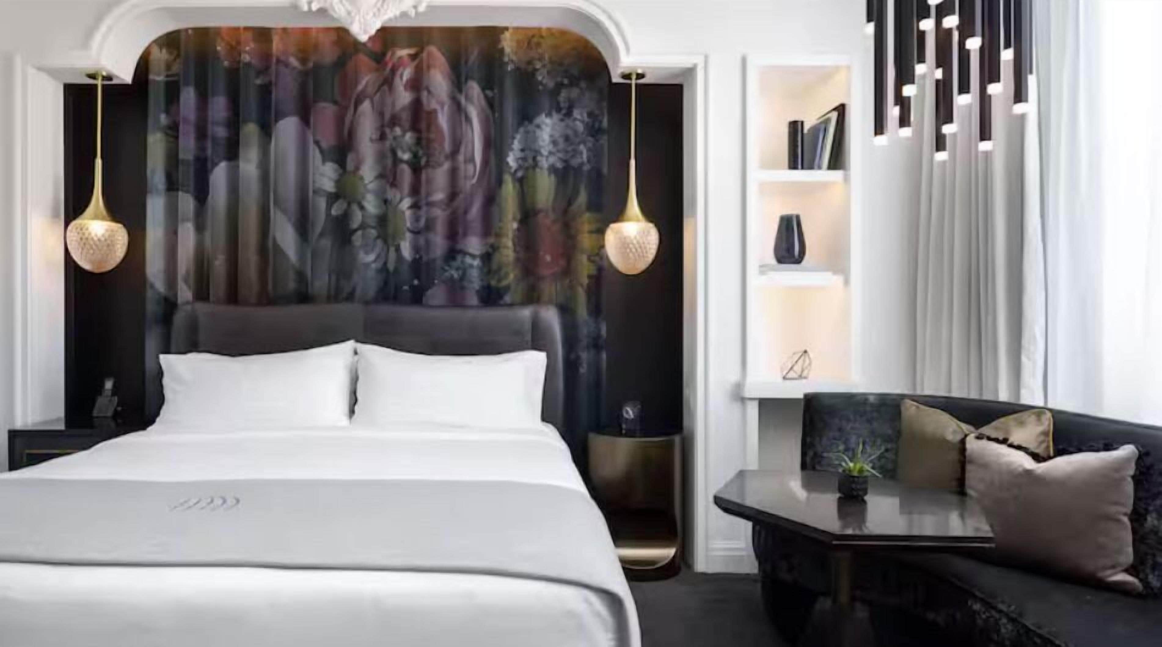 Ein modernes Hotelzimmer mit einem großen Bett, einer Couch, einem Schreibtisch und einer Wand mit floralem Dekor.