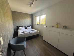 A bedroom with a bed, a chair, a window, and a cabinet.