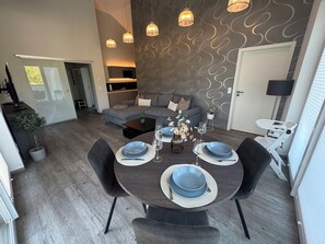 Un coin repas avec une table ronde dressée pour quatre personnes, un canapé gris et un mur orné d’un motif.