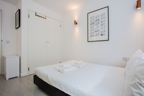A minimalist hotel room with a bed, a framed bicycle illustration, and a white wardrobe.