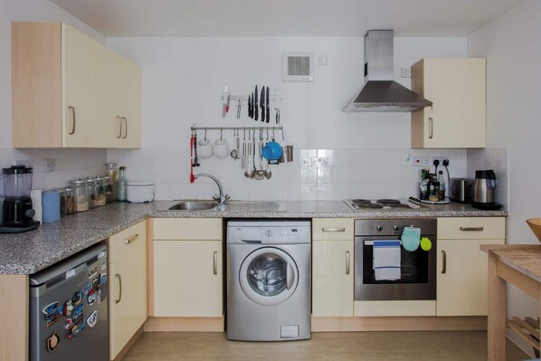 A kitchen with a dishwasher, oven, and various utensils hanging on the wall.
