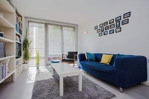 Un salon moderne avec un canapé bleu, une table basse blanche et une bibliothèque.