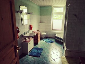Bathroom features a sink, toilet, and bathtub, with a two-tone tile pattern on the walls and a window with blinds.