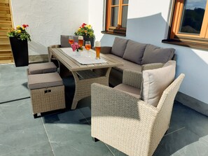 Een terras buiten met rieten meubels, een tafel en potplanten.