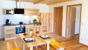 A modern kitchen with wooden cabinets, a built-in oven, and a dining area with a wooden table and benches. - Ferienwohnung Morgensonne, 60 qm Obergeschoss, Separates Schlafzimmer (Söchtenau)