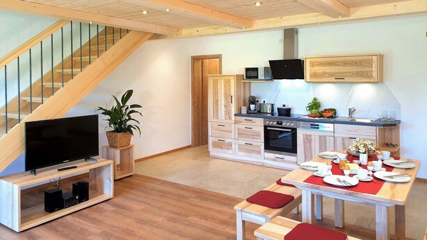 Una cocina moderna con armarios de madera, una mesa de comedor para cuatro personas y una escalera que lleva a un nivel superior.