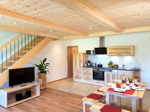 A modern kitchen with wooden cabinets, a dining table set for four, and a staircase leading to an upper level. - Ferienwohnung Abendrot, 86 qm Maisonette, 2 Separate Schlafzimmer (Söchtenau)