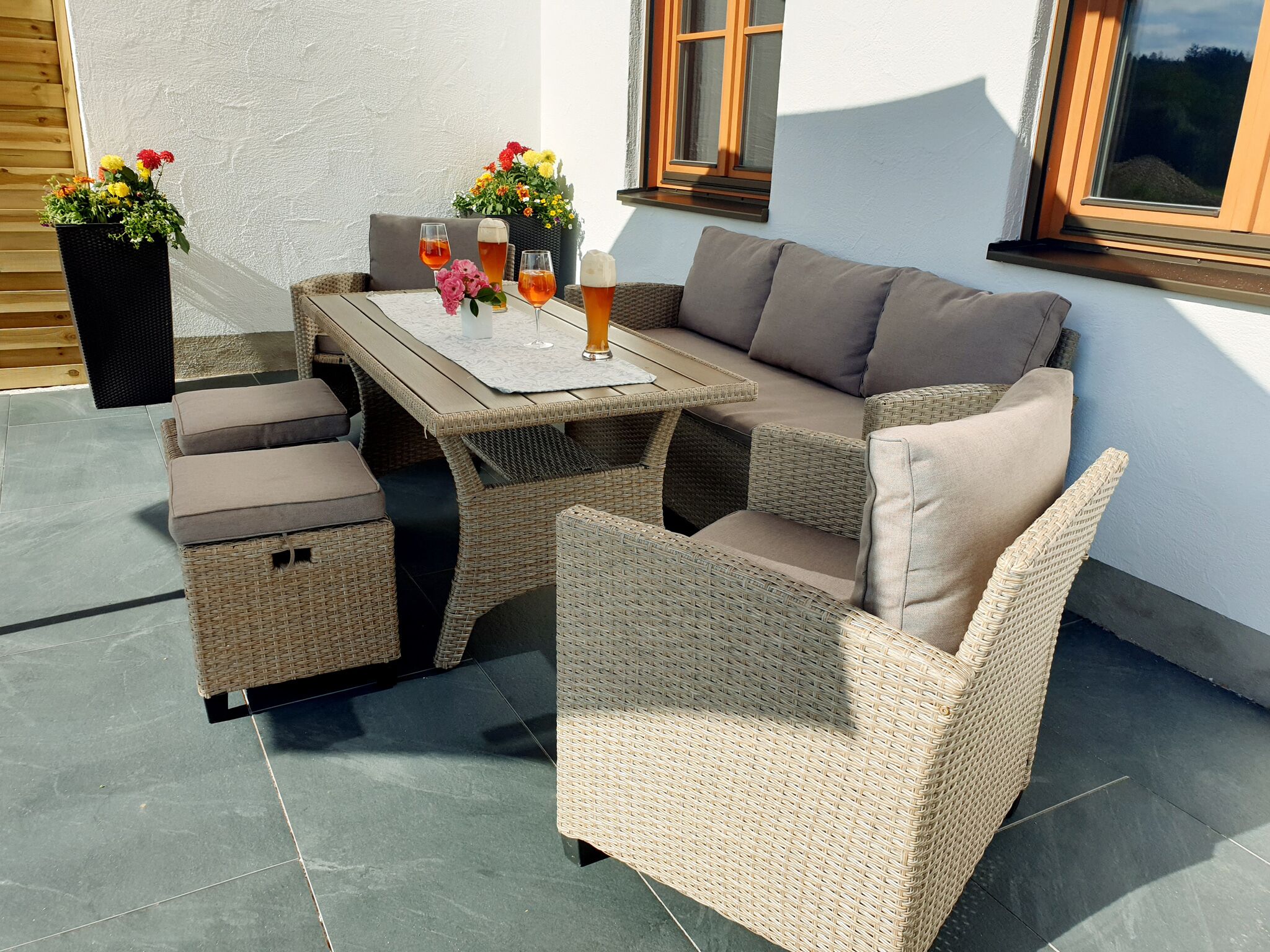 An outdoor patio with wicker furniture, a table, and potted plants.