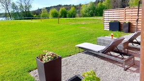 Un patio con mobiliario exterior, una mesa con una bebida y vistas a un lago y un bosque.