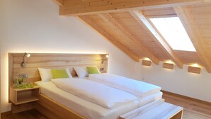 Un dormitorio con techo de madera, tragaluz, cama con ropa blanca y mesitas de noche con lámparas.