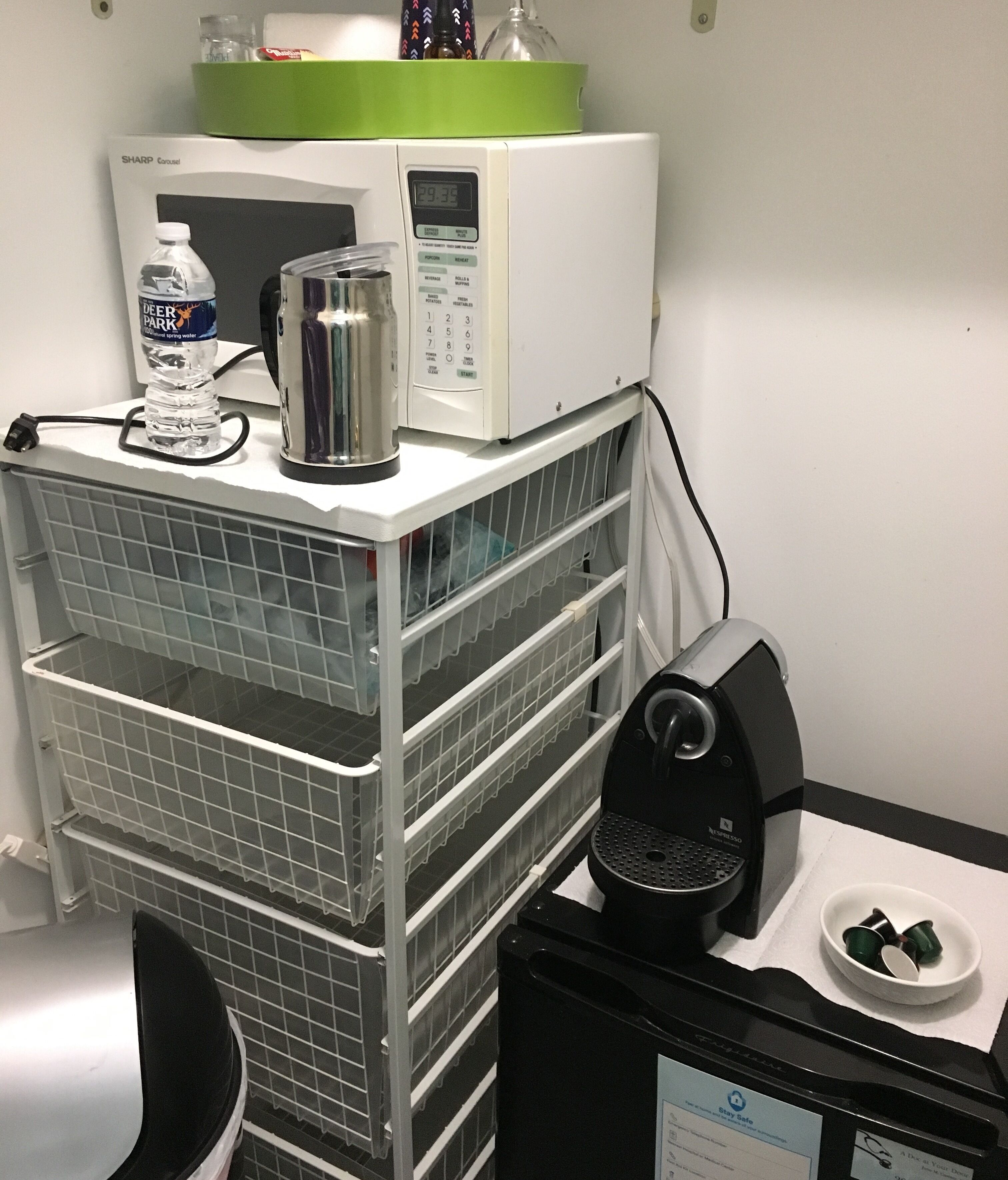 Une petite cuisine équipée d’un four à micro-ondes, d’une machine à café et d’un distributeur d’eau. On y trouve également des étagères de rangement et une autre machine à café sur le plan de travail.