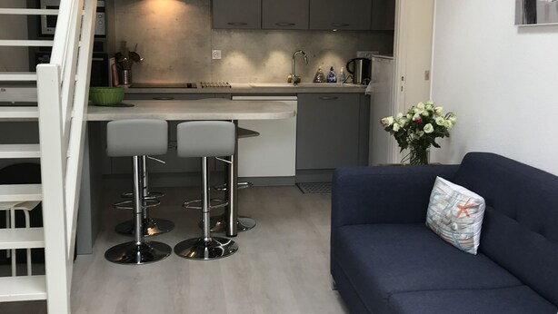 Une cuisine moderne avec des meubles gris, un îlot central et un escalier menant à une mezzanine.