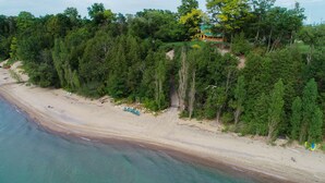 Vue aérienne d’une plage avec une cabane en bois entourée d’une forêt dense.