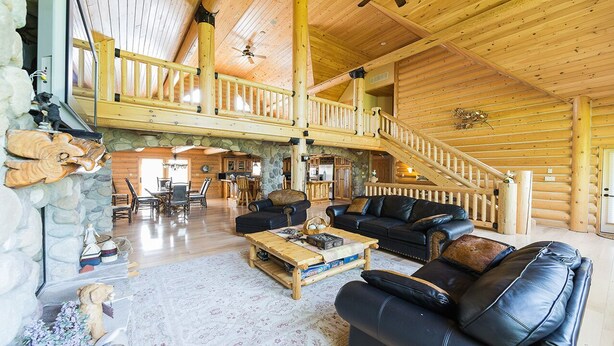 Un intérieur spacieux de chalet en bois, avec un escalier en bois, une cheminée et un coin salon confortable.
