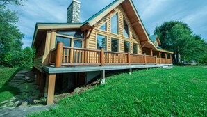 Une cabane en rondins avec une cheminée en pierre, une terrasse en bois et un escalier en pierre menant à l’entrée.