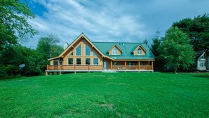 Une grande maison en bois avec un toit vert, un porche à l’avant et une vaste pelouse.
