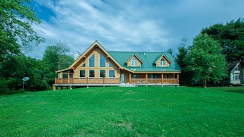 A large wooden house with a green roof, a front porch, and a spacious lawn.