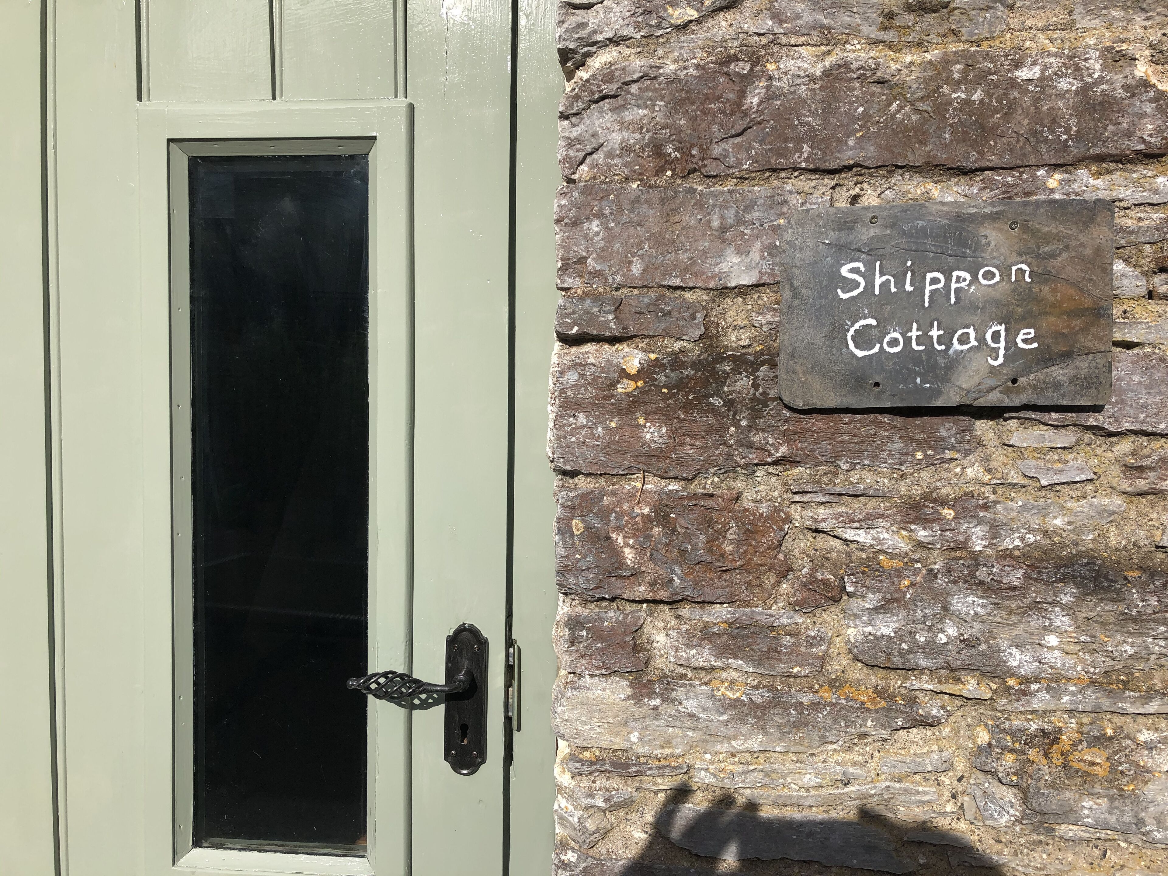 A door with a frosted glass window and a metal handle, and a stone wall with a sign reading "Shippon Cottage".