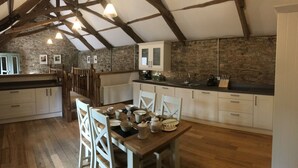 A rustic kitchen with wooden beams, white cabinets, and a dining table set for four. - Two bedroom stone cottage near Dartmoor and Devon beaches (Ashburton)