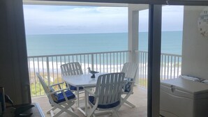 Uma varanda com mesa e cadeiras, vista para a praia e um quadro branco com números.