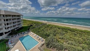 Um hotel com piscina, vista para a praia e um edifício grande com varandas.