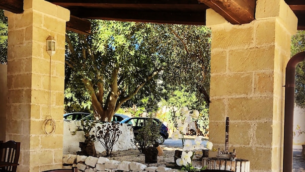An outdoor dining area with a stone wall, wooden chairs, and a table set for two. - Borgo Santuri (Ostuni)
