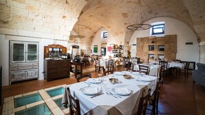 A spacious dining area with high stone walls and arched ceilings, featuring multiple tables set for dining. - Borgo Santuri (Ostuni)