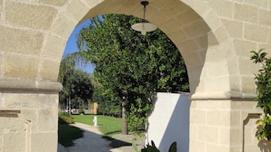 An arched stone doorway leading to a courtyard with a white wall, a ceiling fan, and a cactus plant. - Borgo Santuri (Ostuni)
