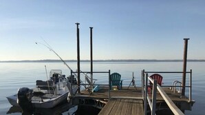 Eine Holzstege, der sich in ruhiges Wasser erstreckt, mit Angelrute, einem kleinen Boot und zwei Stühlen.
