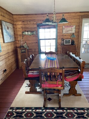 A wooden dining room with a large table, chairs with colorful cushions, a vintage radio, and a map on the wall.