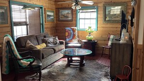 Ein gemütliches Wohnzimmer mit Holzboden, einer Couch, einem Glastisch und einem Deckenventilator.