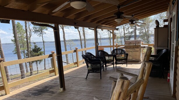 Eine Holzterrasse mit Gartenmöbeln, Blick auf den See und ein überdachter Bereich mit Deckenventilator.