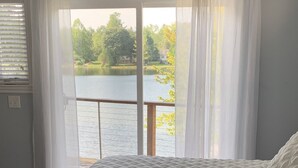 A bedroom with a large bed, a view of a lake, and a window with sheer curtains. - Relaxing Oxford Retreat (Oxford)