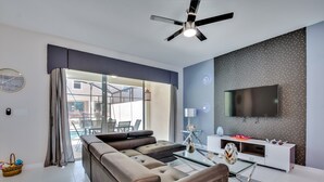 A modern living room with a sectional sofa, a glass coffee table, a white entertainment unit, and a ceiling fan. - South-Facing Pool & Spa • No Rear Neighbors • Game Room • Near Disney (Kissimmee)
