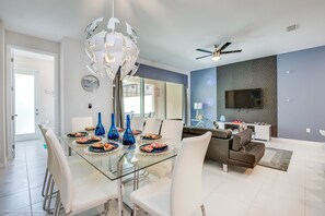 Un espace repas moderne avec une table en verre, des chaises blanches et des vases bleus.