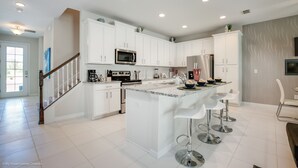 A modern kitchen with white cabinetry, a central island with bar stools, stainless steel appliances, and recessed ceiling lighting. - South-Facing Pool & Spa • No Rear Neighbors • Game Room • Near Disney (Kissimmee)