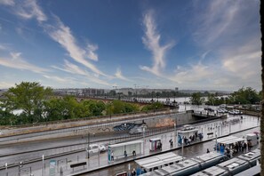 A riverside walkway with a bridge in the background, a covered waiting area, and a view of the river. - LE RICHELIEU - Magnifique duplex avec une vue Incroyable (Bordeaux)