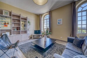 A living room with a sofa, a coffee table, a TV, and a bookshelf. - LE RICHELIEU - Magnifique duplex avec une vue Incroyable (Bordeaux)