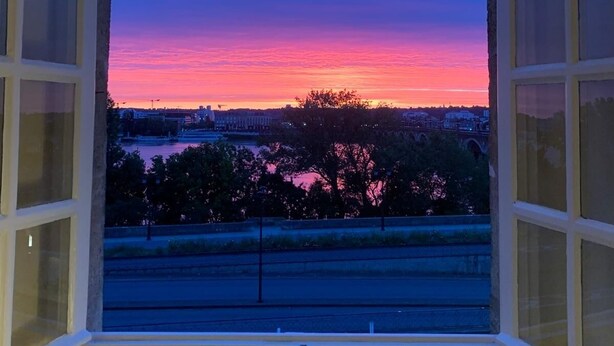A room with a large window offering a view of a sunset over a cityscape. - LE RICHELIEU - Magnifique duplex avec une vue Incroyable (Bordeaux)
