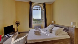 A hotel room with a bed, a TV, a fan, and a window with curtains. - LE RICHELIEU - Magnifique duplex avec une vue Incroyable (Bordeaux)