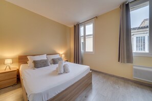 A neatly made bed with white linens and two pillows, a bedside lamp, and a window with curtains. - LE RICHELIEU - Magnifique duplex avec une vue Incroyable (Bordeaux)