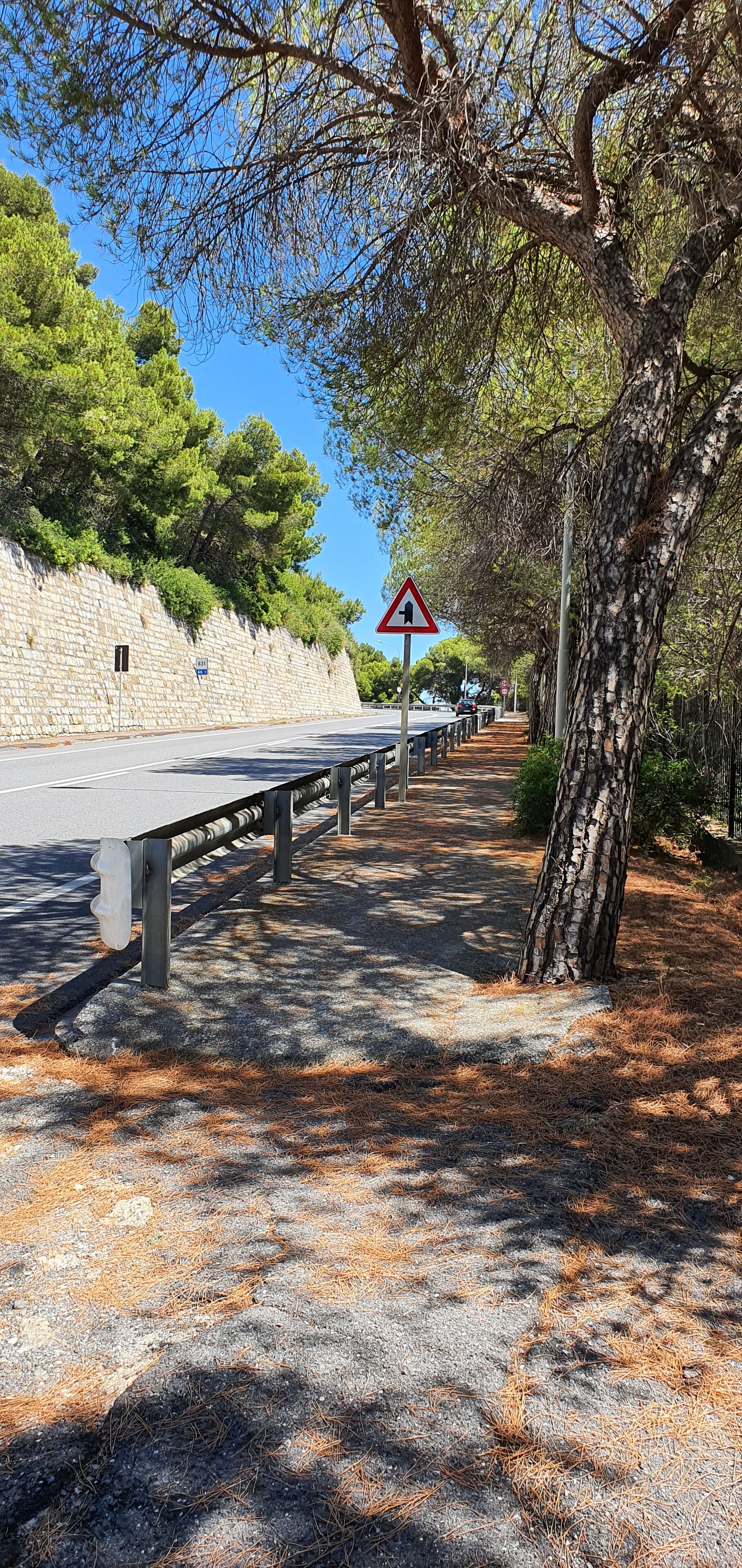 A road with a stone wall on one side and a tree-lined path on the other.