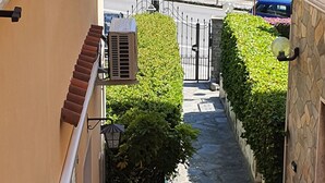 Un vialetto stretto con vista sul mare, un muro di pietra e un cancello che dà su una strada.