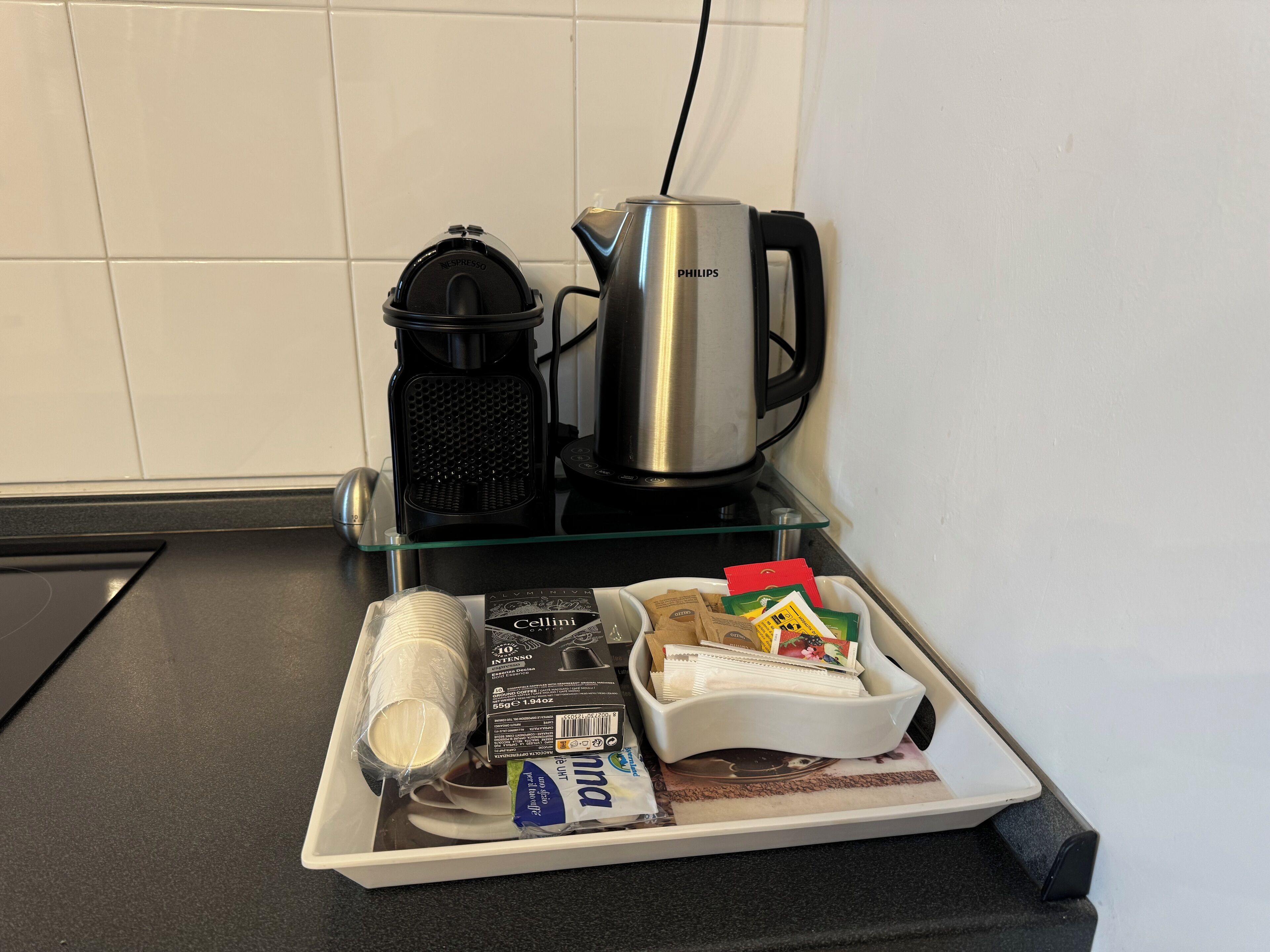 A kitchen counter with a coffee maker, a kettle, and a tray with coffee pods and a milk carton.