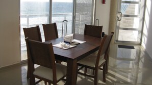 Un espace repas avec une grande table et des chaises, un extincteur fixé au mur, et une vue sur la mer grâce à de grandes fenêtres.