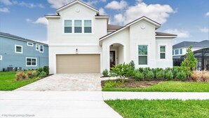 A two-story house with a beige garage door, a small front porch, and a well-maintained lawn. - Private Splash Pool • Disney Room • Game Room • Near Disney • Resort (Kissimmee)