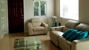 A living room with a wooden ceiling, two sofas, a glass coffee table, and a door.