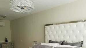 A bedroom with a tufted headboard, a grey patterned bedspread, and a grey throw blanket.