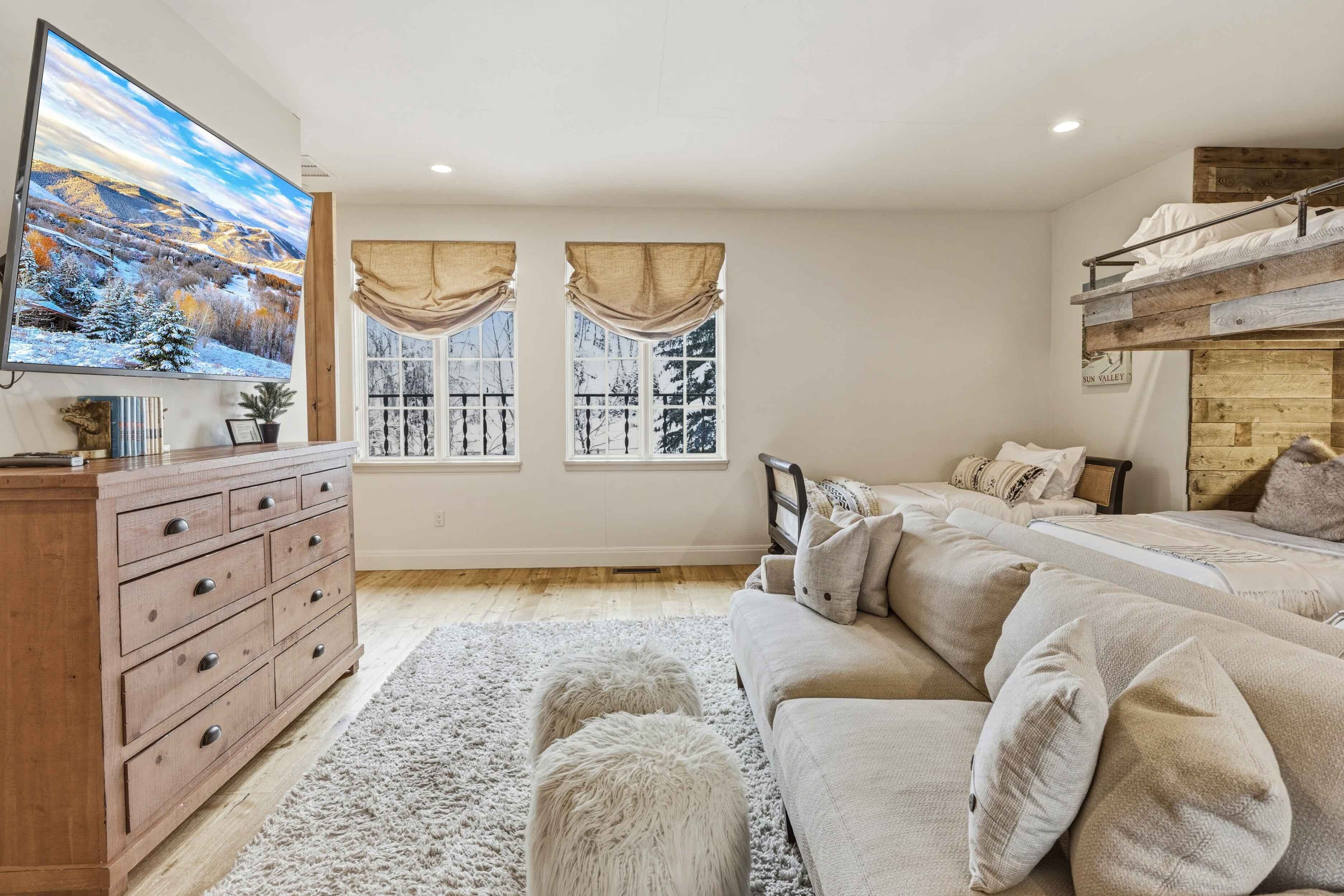 A cozy bedroom with a large bed, a TV, a dresser, and two windows with curtains.