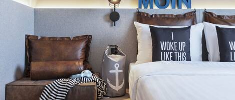 A hotel room with a bed, a bench with pillows, a wall-mounted light, and a large 'MOIN' sign.